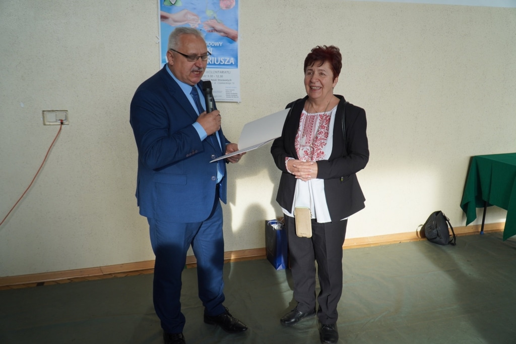 Mężczyzna w garniturze wręcza nagrodę kobiecie podczas gali wolontariatu.