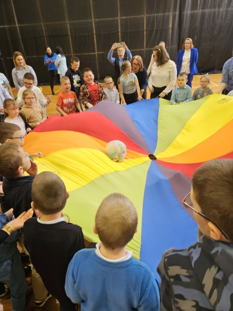 Dzieci bawią się kolorowym spadochronem podczas finału konkursu „Niebieskie Motyle”