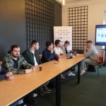 Uczestnicy konferencji RIPE 90 przy stole dyskutują na tle ekranu z prezentacją.
