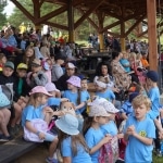 Dzieci na pikniku "Zdrowo rosnę z KOWR" w Radawie, siedzą pod zadaszeniem.