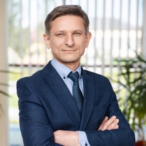 Dariusz Kłak w granatowym garniturze ze skrzyżowanymi ramionami