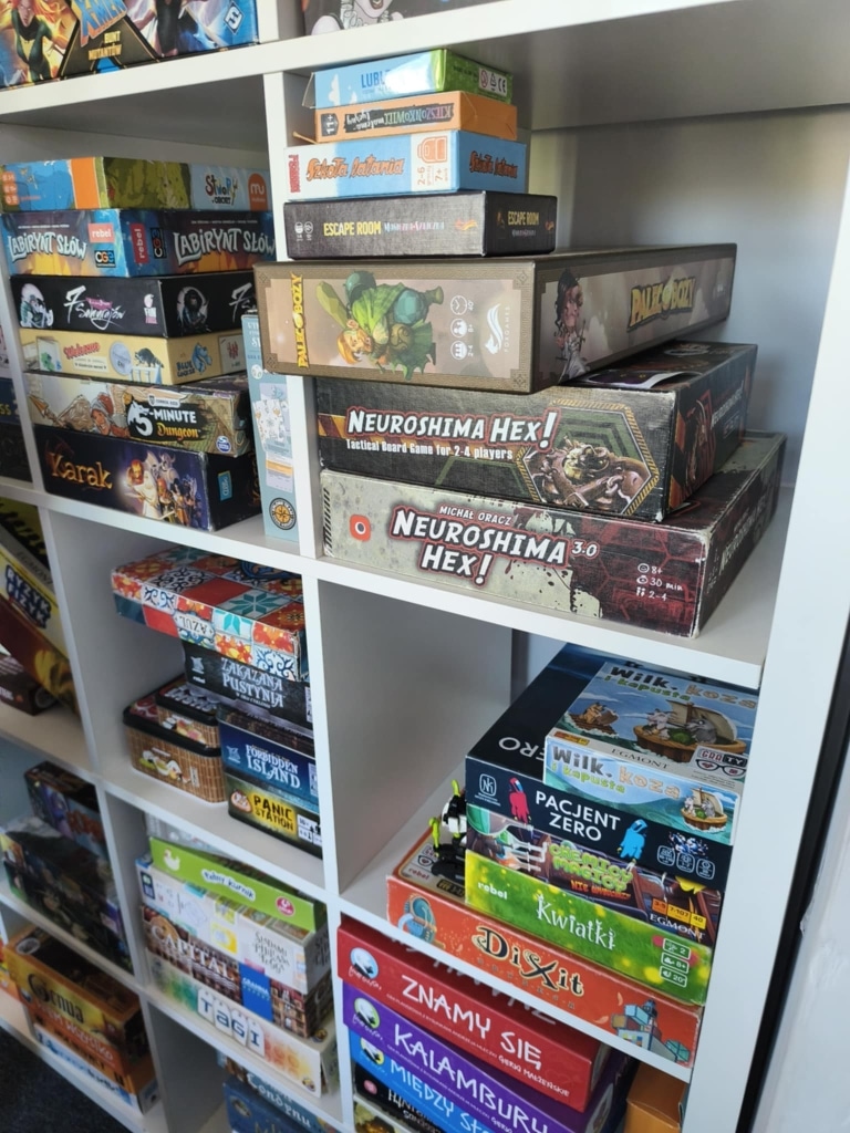 Półki pełne gier planszowych, w tym Escape Room i Neuroshima Hex.