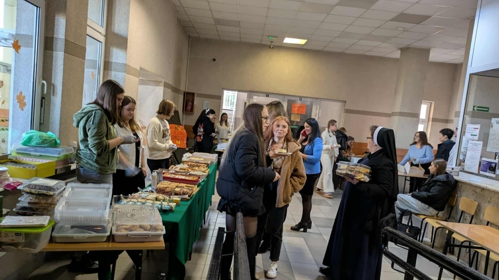 Kiermasz ciast na Wydziale Humanistycznym PANS w Jarosławiu: studenci i siostra zakonna przy stołach z wypiekami.