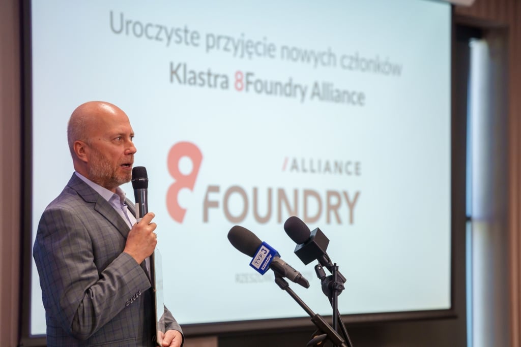 Mężczyzna przemawia na tle ekranu z logo Klastra 8Foundry Alliance