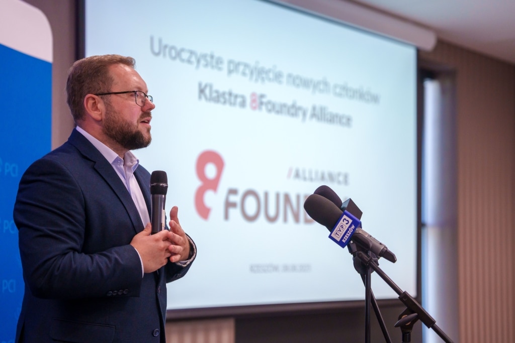 Mężczyzna w garniturze przemawia na tle ekranu z logo Klastra 8Foundry Alliance