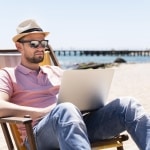 Mężczyzna w kapeluszu pracuje na laptopie na plaży w Niemczech