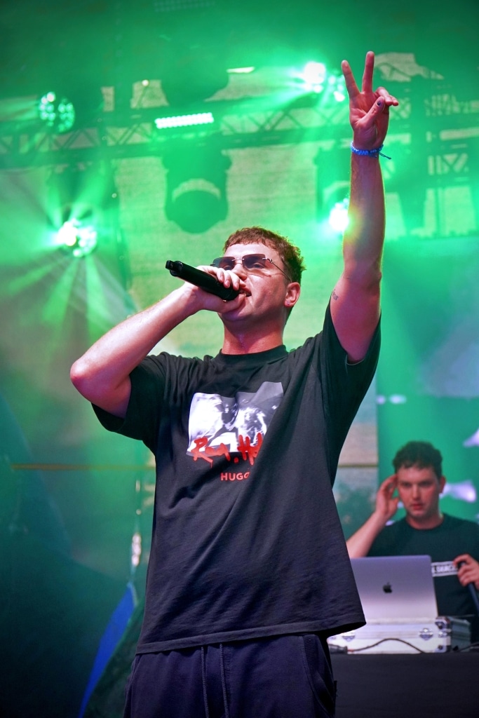 Raper z Polski na Juwenaliach 2025, pozdrawia publiczność znakiem pokoju.