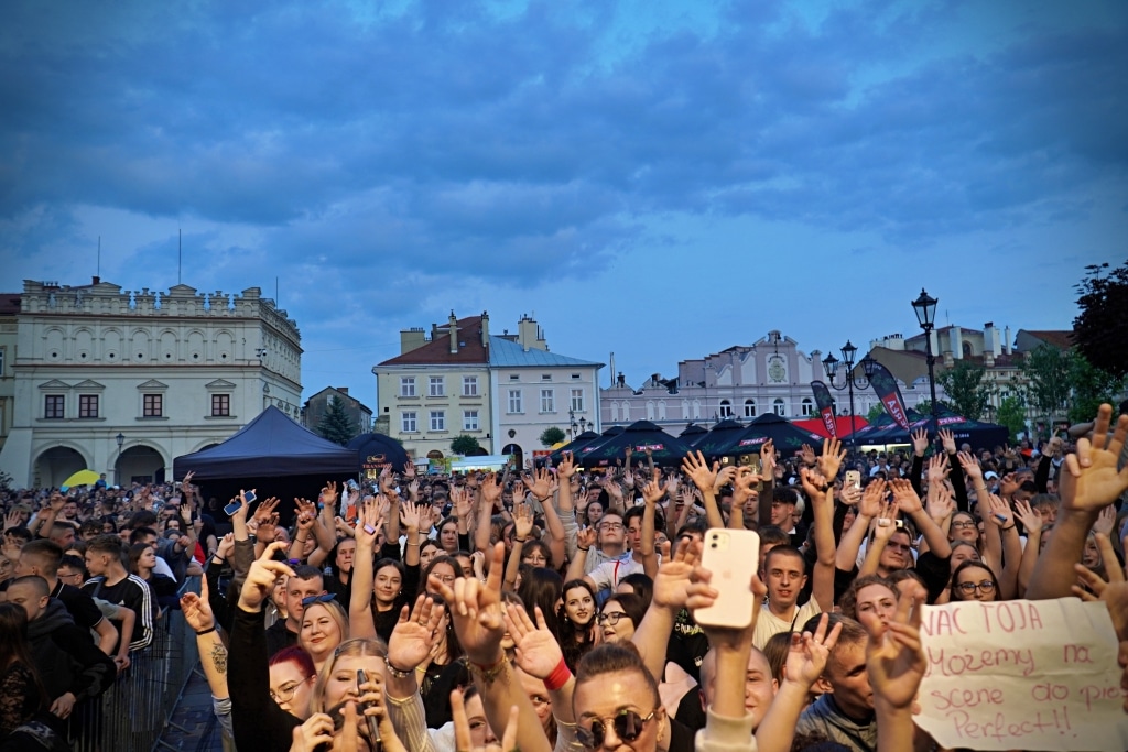 Tłum ludzi na Juwenaliach 2025, ręce w górze, budynki w tle.