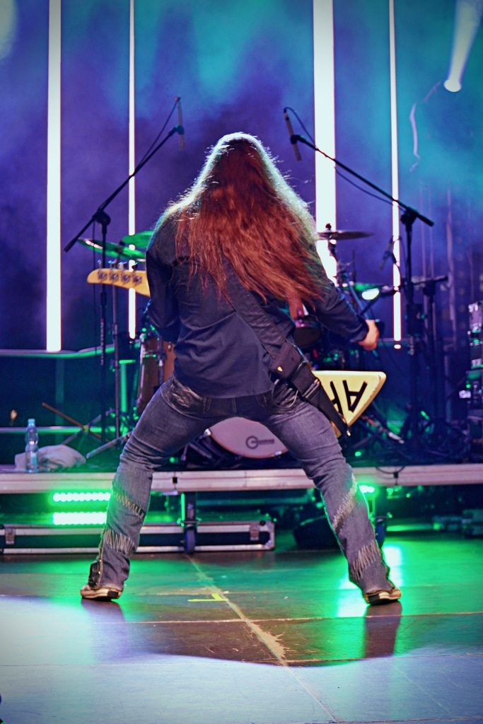 Długowłosy gitarzysta na scenie Juwenalia 2025 z zespołem rockowym.