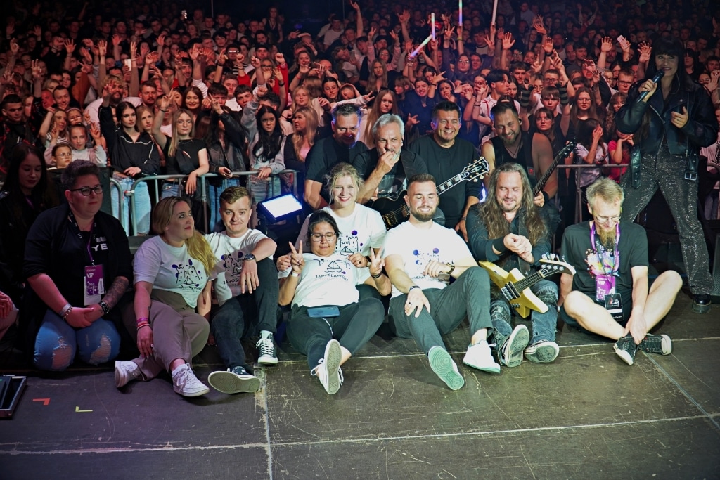 Grupa fanów Juwenaliów 2025 pozuje na scenie z zespołem muzycznym.