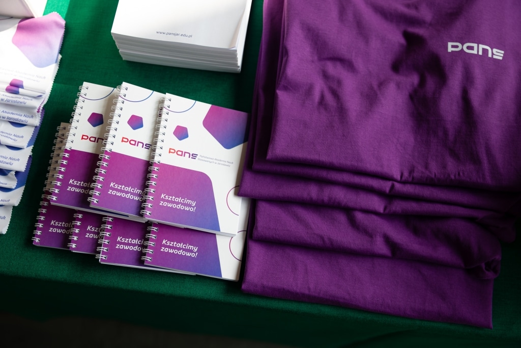 Materiały promocyjne PANS: zeszyty i koszulki na Dzień Otwarty 2025.