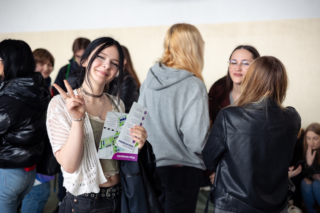 Uśmiechnięta dziewczyna z materiałami informacyjnymi na Dzień Otwarty 2025.