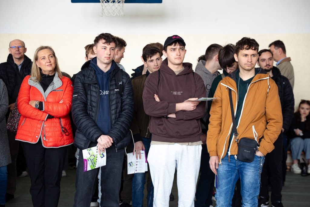 Uczestnicy Dnia Otwartego 2025 stoją w kolejce, niektórzy trzymają materiały informacyjne.