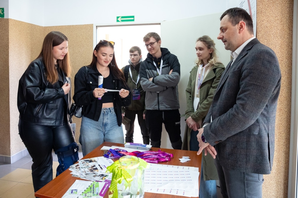 Grupa młodych ludzi na Dniu Otwartym 2025 przy biurku z materiałami informacyjnymi.