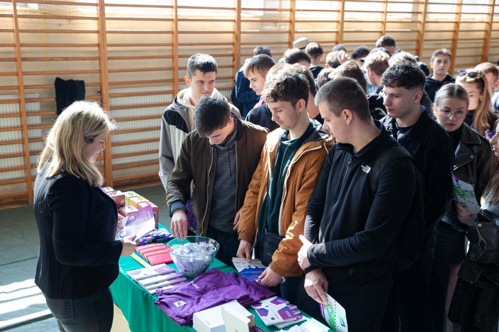 Uczestnicy Dnia Otwartego 2025 przy stoisku informacyjnym z materiałami promocyjnymi.