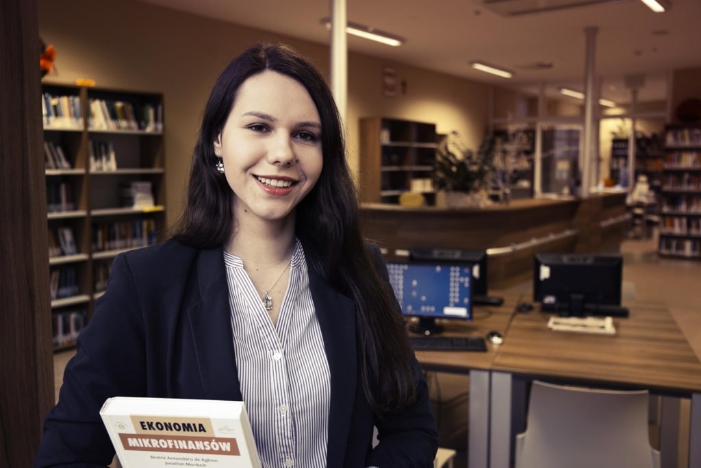 Studentka z książką "Ekonomia Mikrofinansów" w bibliotece