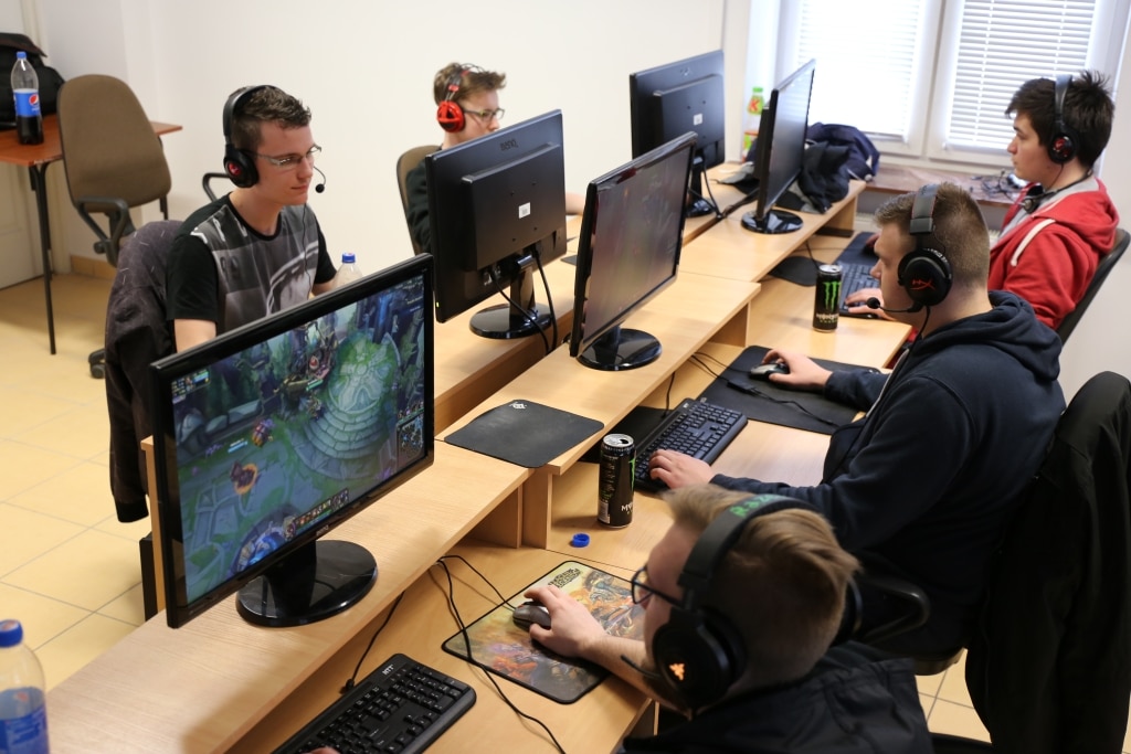 Gracze e-sportowi w akcji na stanowiskach komputerowych w bazie dydaktycznej.