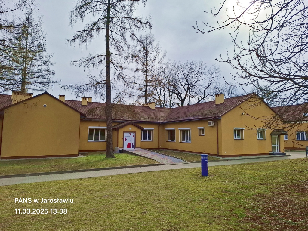 Żółty budynek PANS w Jarosławiu z drzewami i trawnikiem