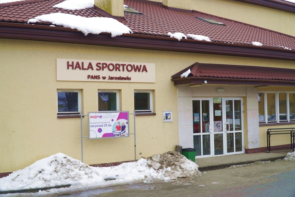 Hala sportowa PANS w Jarosławiu zimą, z tablicą informacyjną.