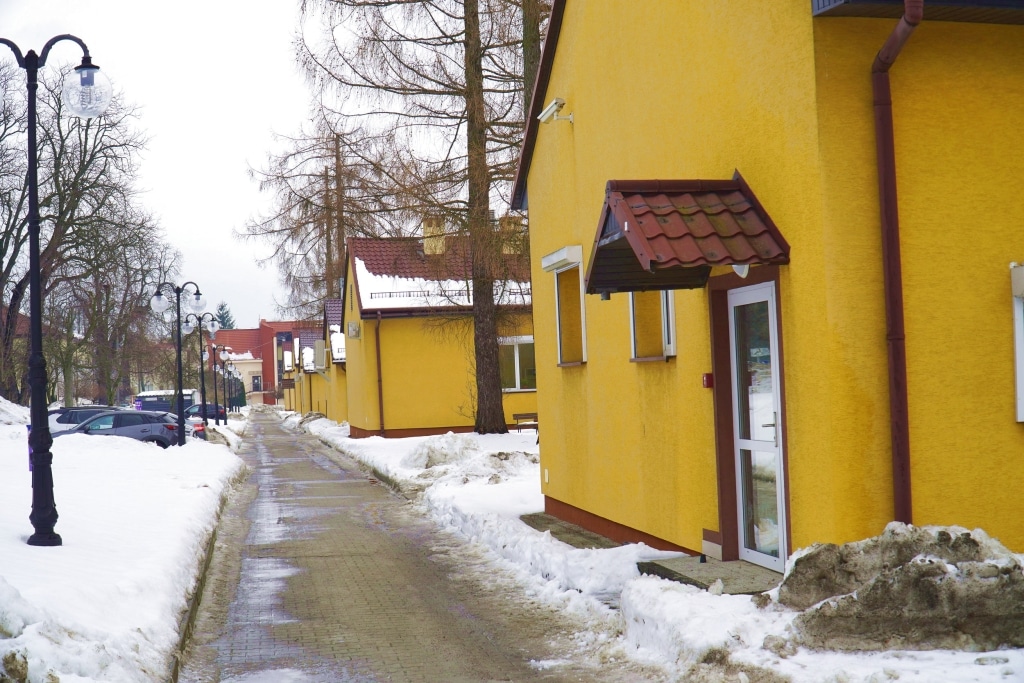 Zimowy kampus PANS w żółtych budynkach i ośnieżonej ścieżce