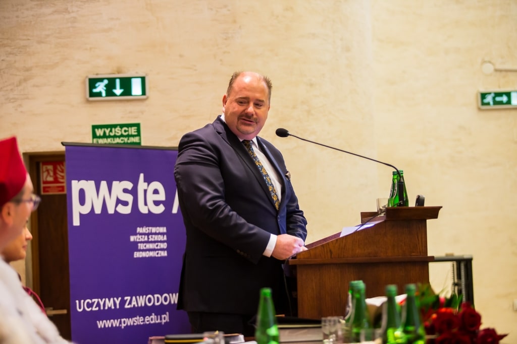 Mężczyzna w garniturze przy mównicy podczas inauguracji PWSZ te