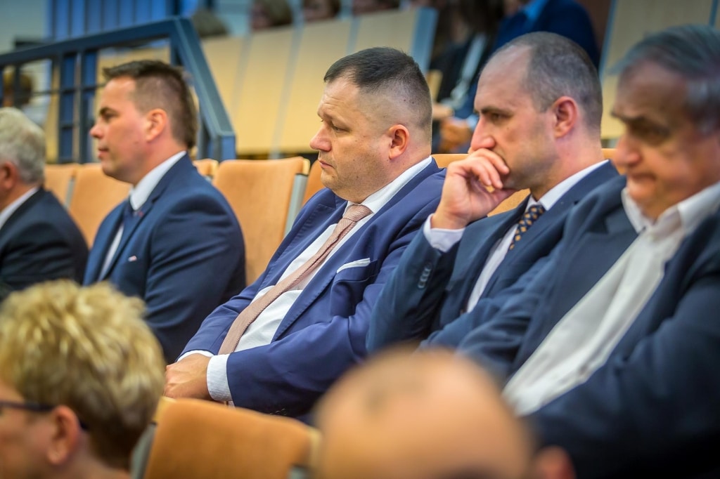 Uczestnicy Inauguracji 2018/2019 w garniturach, siedzący w sali konferencyjnej.