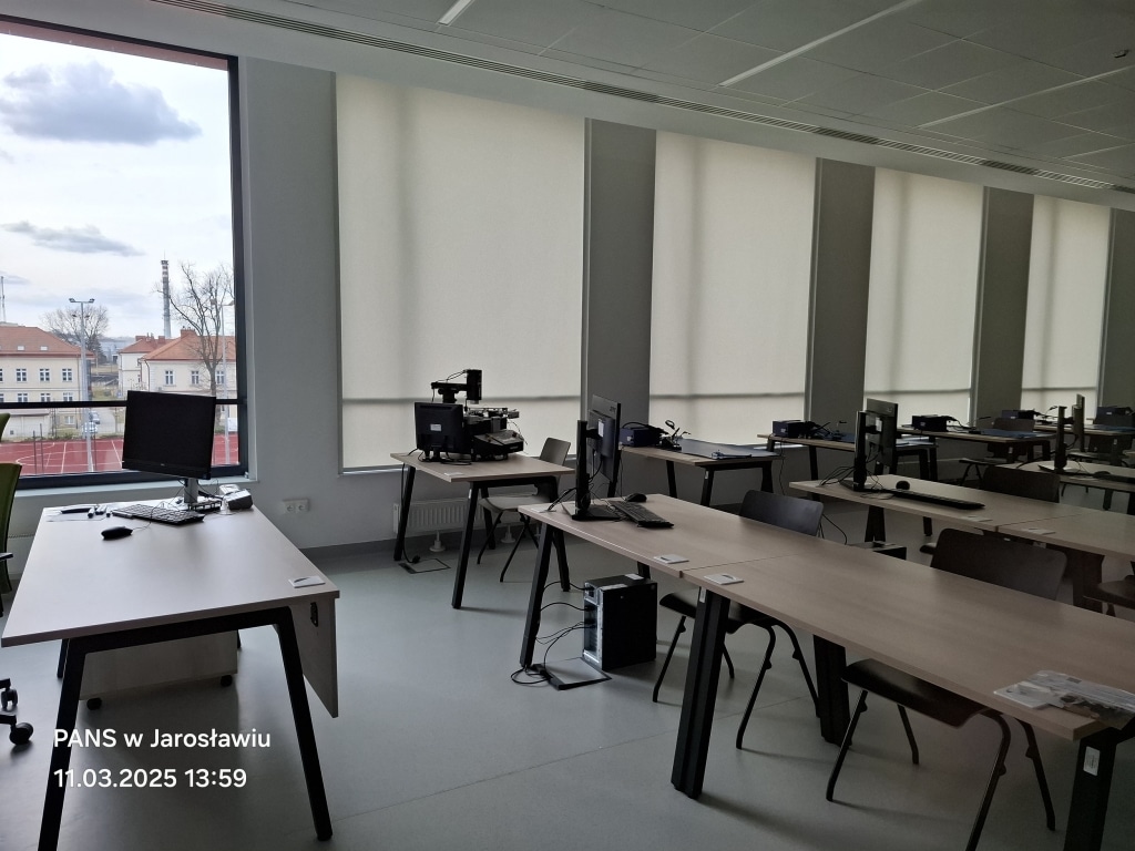 Nowoczesna sala komputerowa z biurkami, komputerami i dużym oknem w PANS w Jarosławiu.